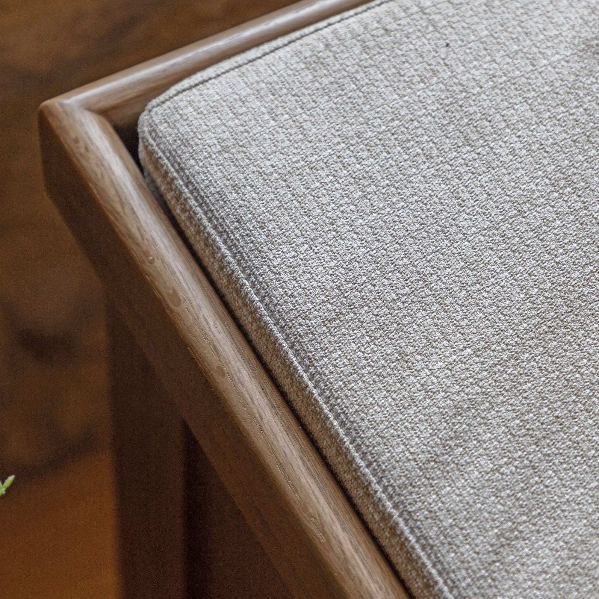A close-up view of the corner of the cushioned top on the wooden storage bench.