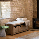 A wooden storage bench with a cushioned top, wicker baskets, and a throw blanket in a room.