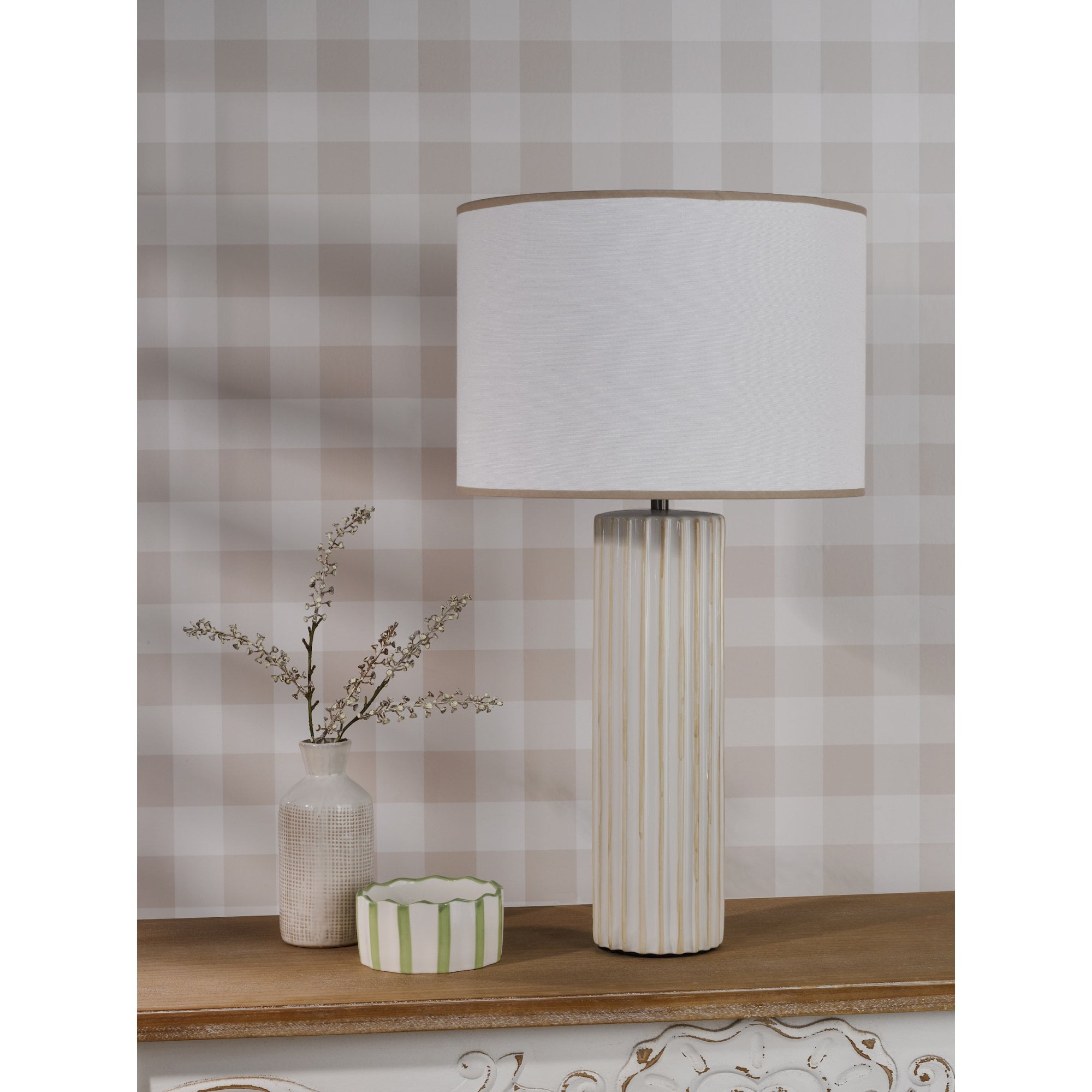 A white fluted table lamp, small vase, and striped box on a wooden shelf.