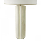 Close-up of the white fluted base of a table lamp with a cream shade.