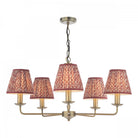 A brass five-arm chandelier with red patterned fabric shades against a white background.