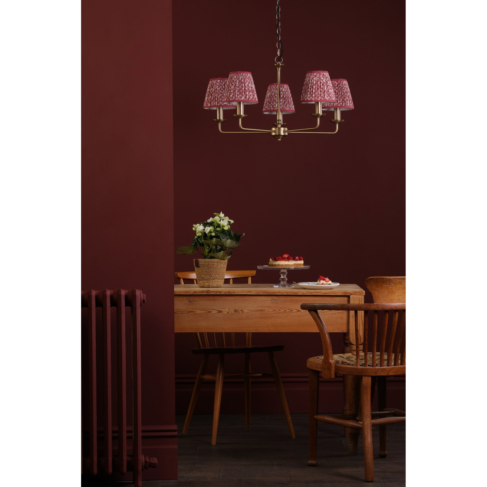 A five-arm chandelier with red patterned shades illuminating a dining room with a table.
