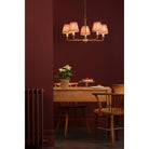 A five-arm chandelier with red patterned shades illuminating a dining room with a table.