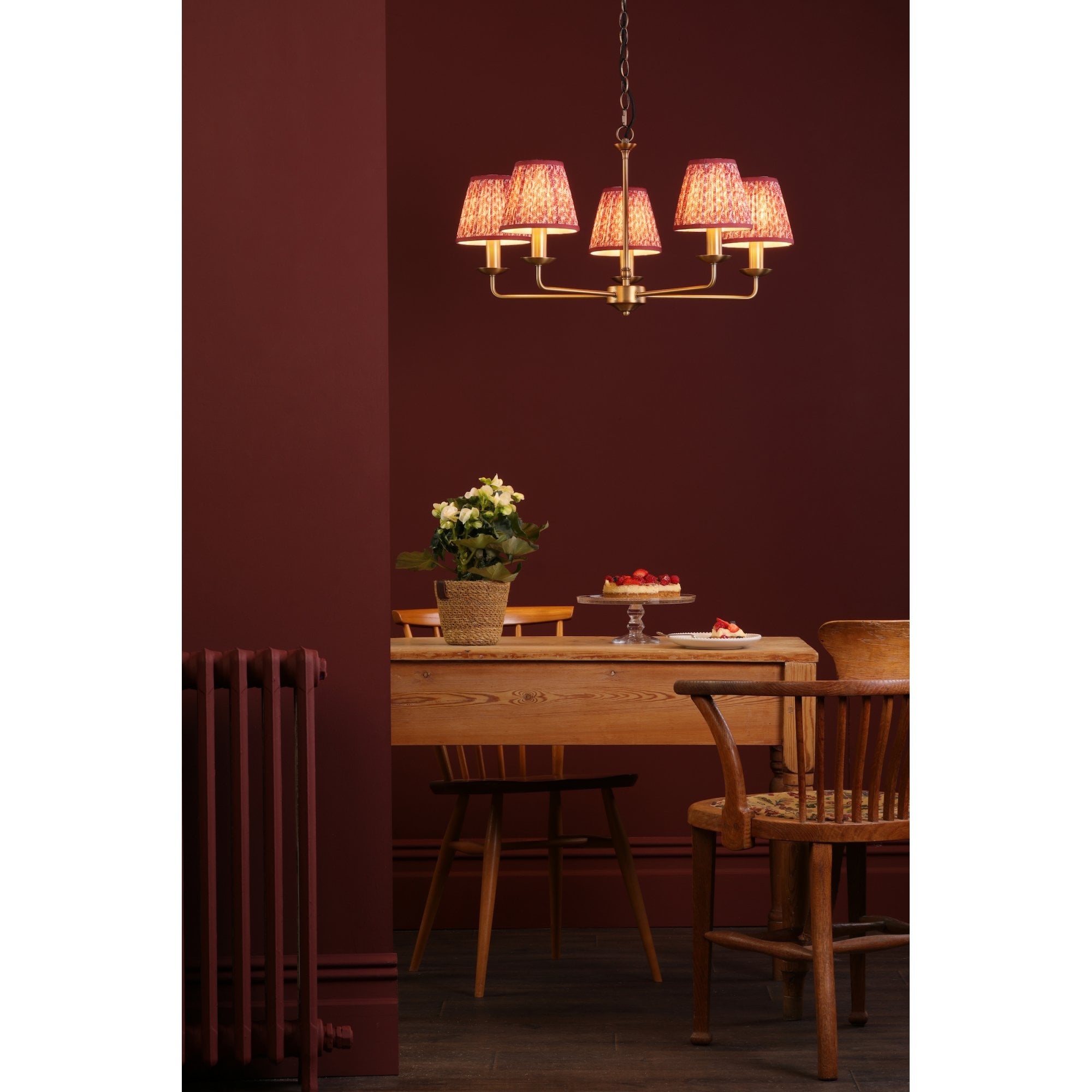 A five-arm chandelier with red patterned shades illuminating a dining room with a table.