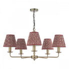 A brass five-arm chandelier with red patterned fabric shades against a white background.