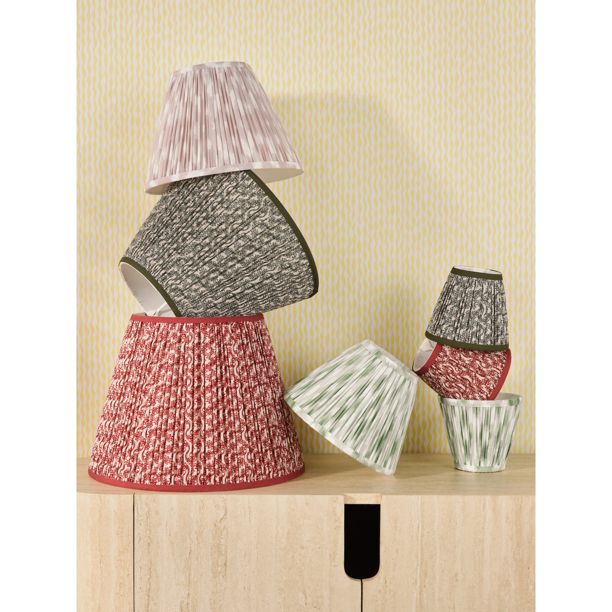 A collection of pleated lamp shades in various sizes and patterns, on a wooden surface.
