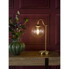 Table lamp on a side table with a vase of flowers, in front of a maroon paneled wall.