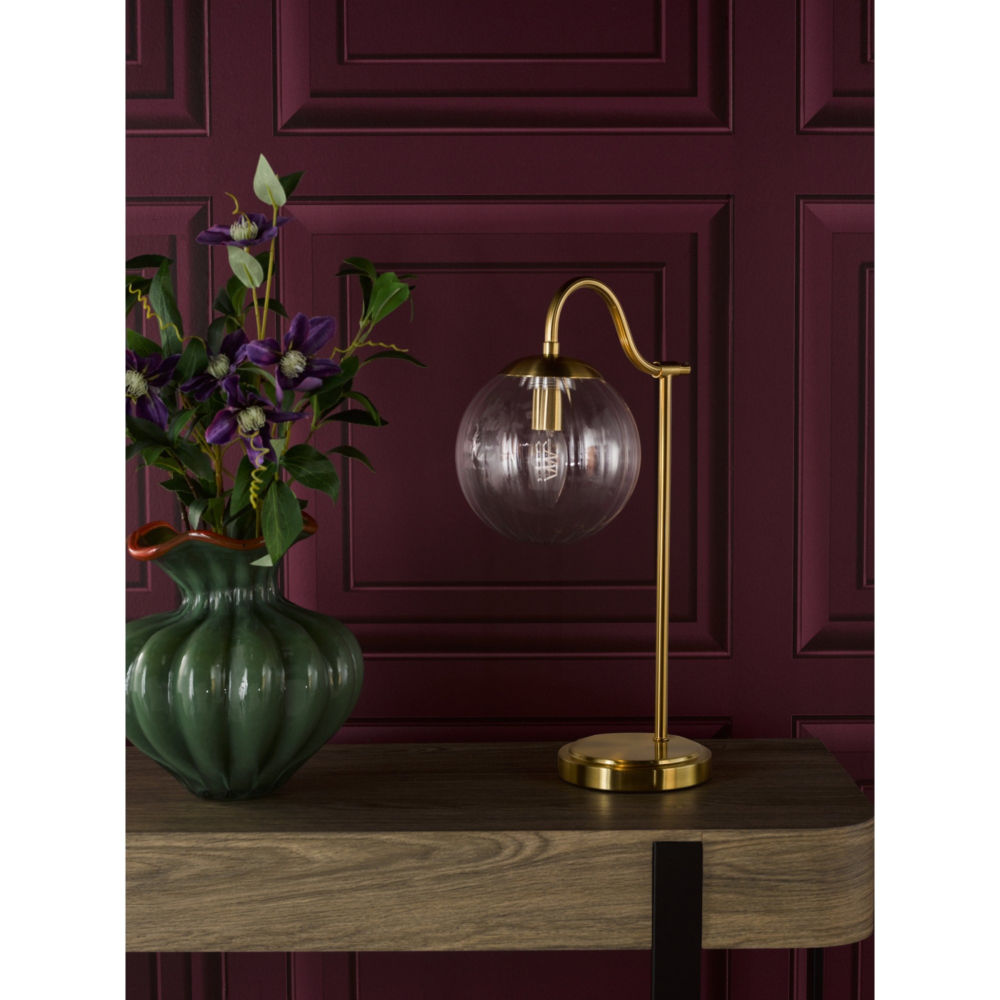 A table lamp with a brass finish and a clear glass shade next to a green vase.
