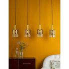 Four gold and clear glass pendant lights hanging over a wooden cabinet with a vase of flowers.