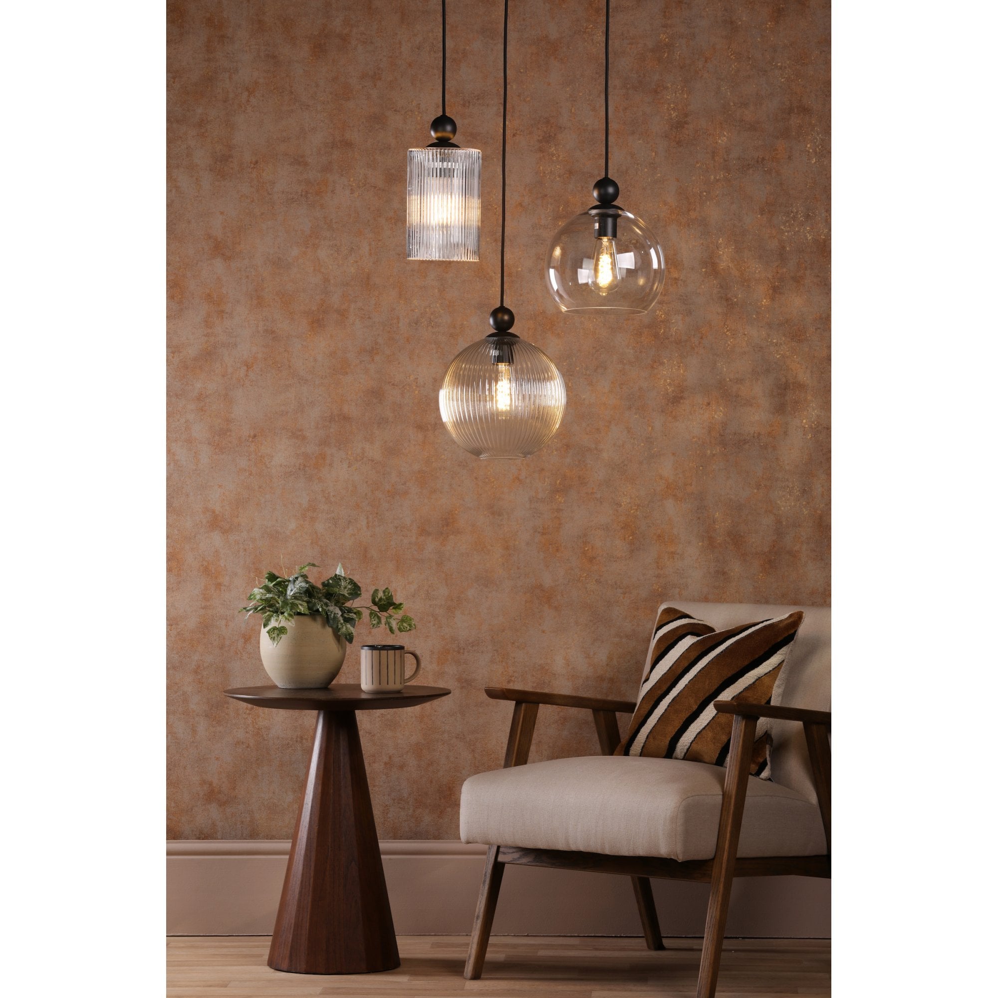 Three pendant lights in a warm-toned room with a chair and side table.