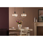 Two glass pendant lights illuminating a dining table with flowers and chairs.