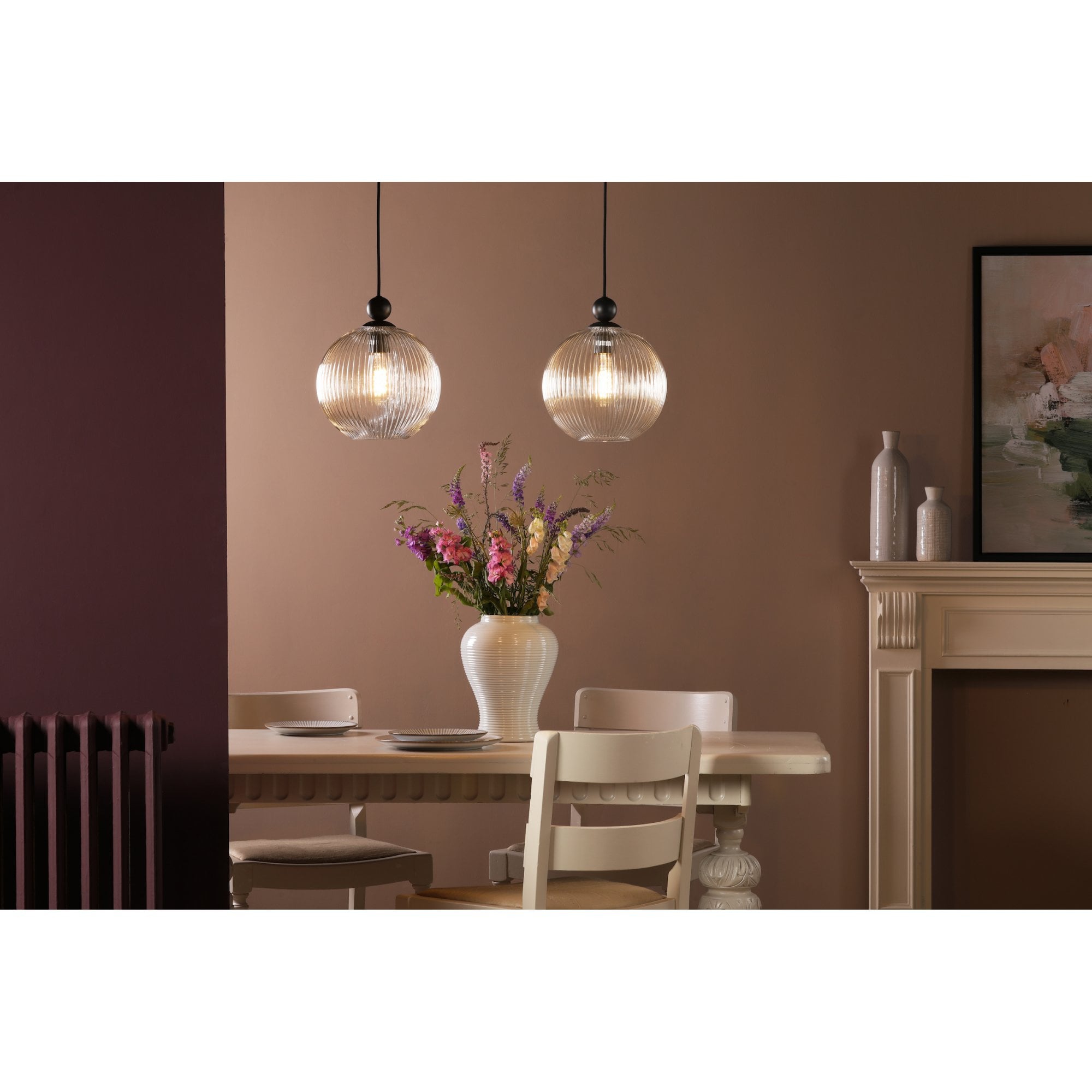 Two glass pendant lights illuminating a dining table with flowers and chairs.
