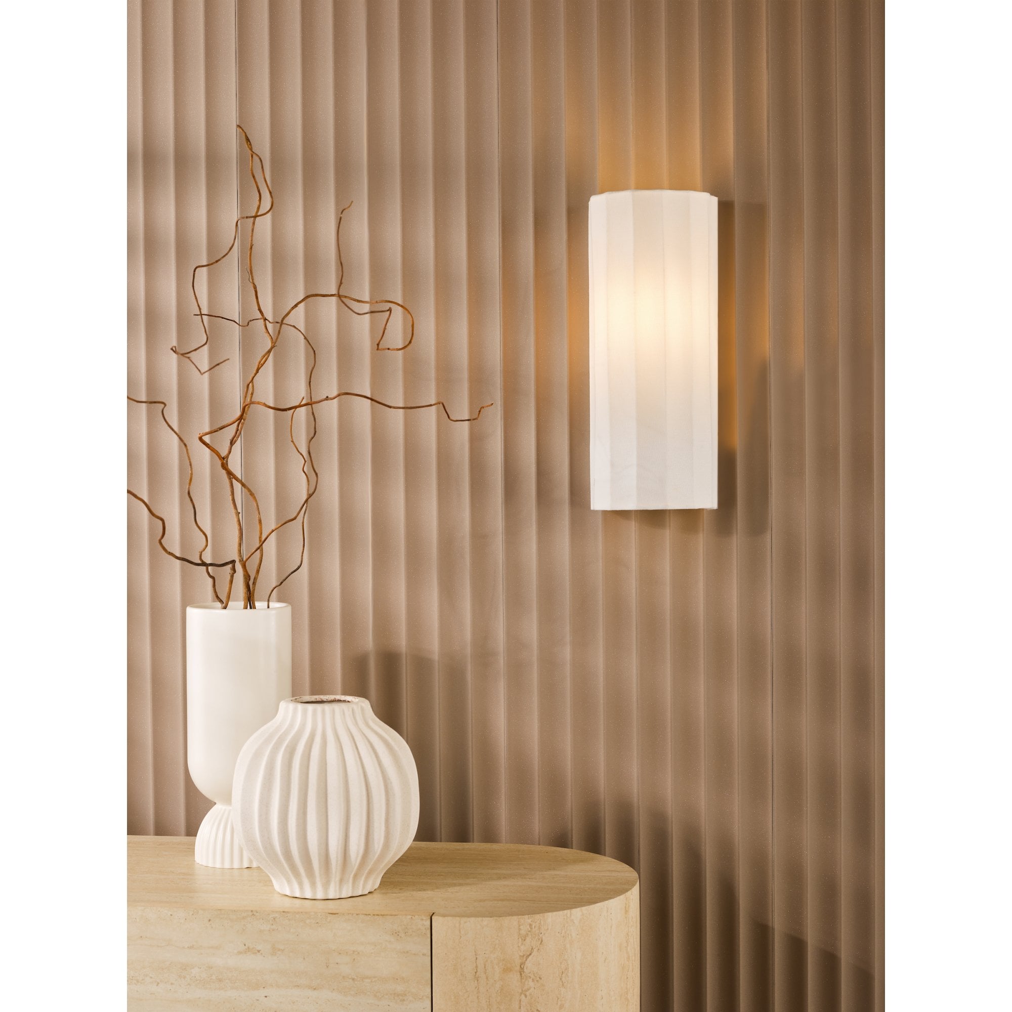 A white fluted wall light illuminates a textured brown wall above a console table with vases.