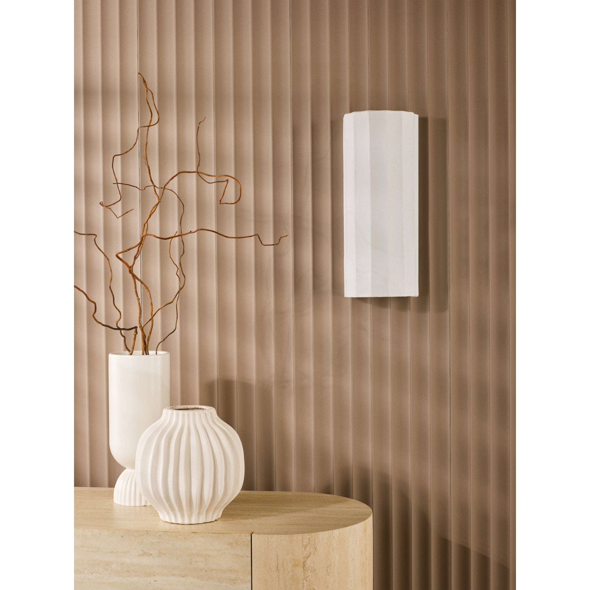 A white fluted wall light on a textured brown wall, with decorative vases on a table.