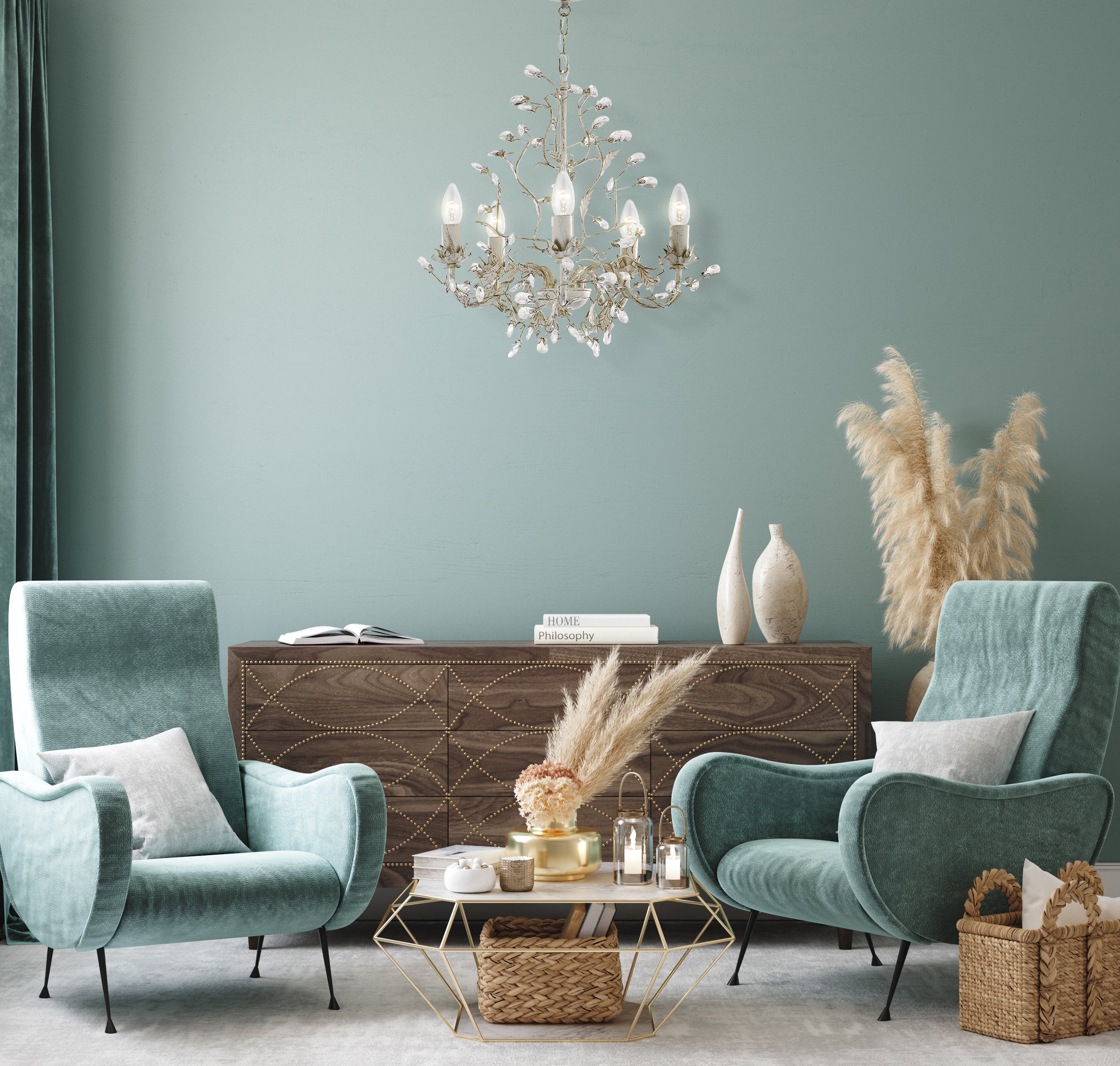 A chandelier illuminating a stylish living room with teal armchairs and a wooden cabinet.