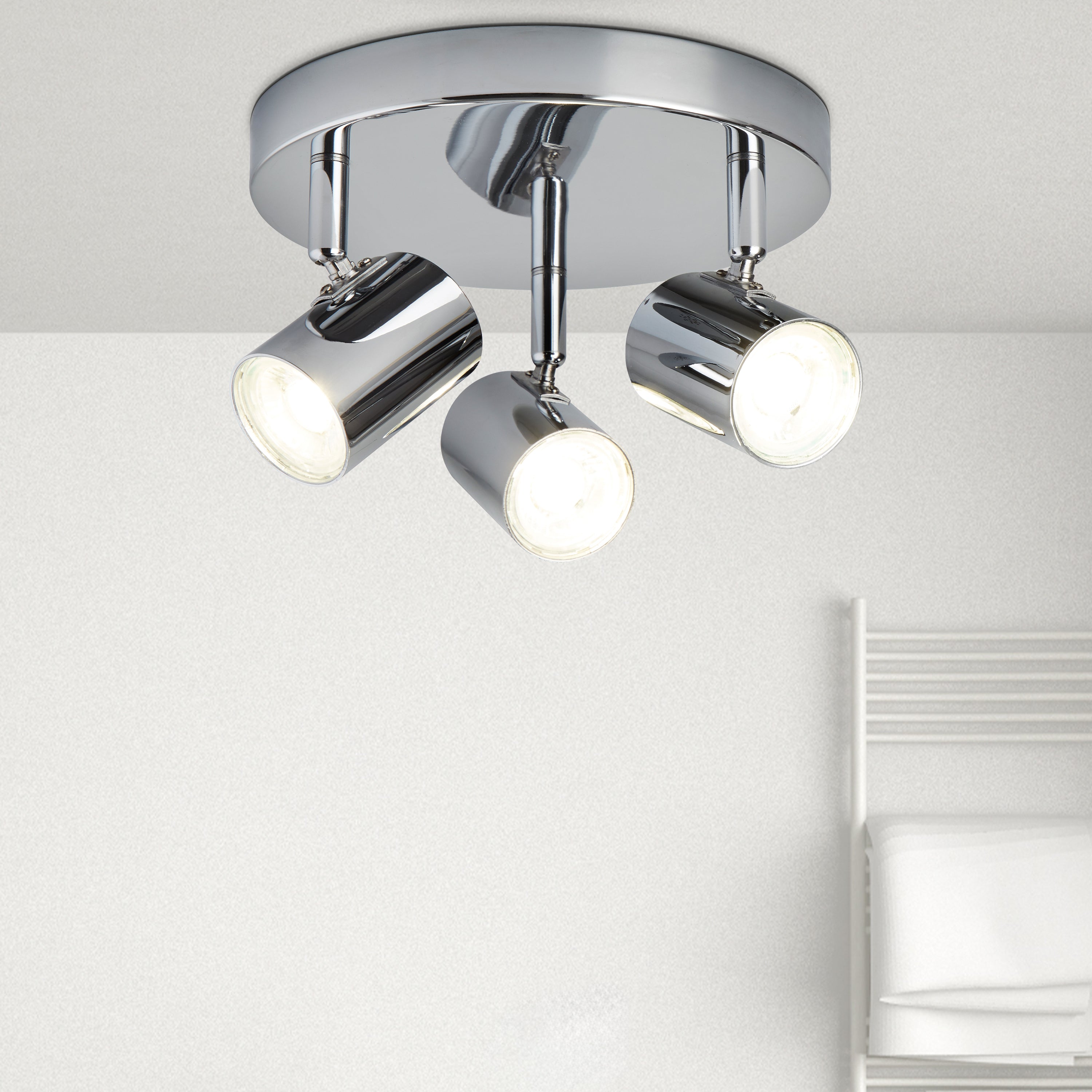 A chrome ceiling light with three spotlights installed in a modern bathroom setting.