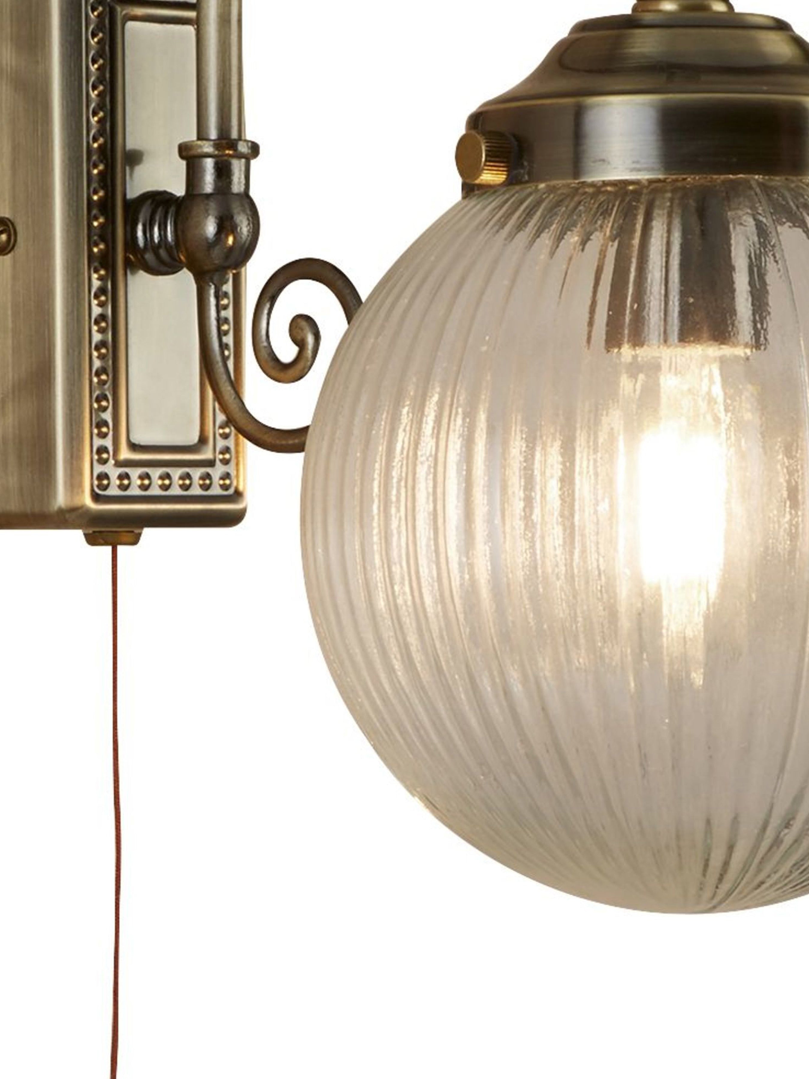 Close-up of a vintage brass wall light showing the ribbed glass globe and pull cord.
