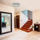 The crystal ceiling light illuminates a modern foyer with a large mirror and wooden staircase.