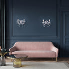 Two crystal wall sconces illuminating a dark blue wall above a pink sofa.