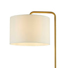 A close-up of a floor lamp's cream drum shade, showing the light-diffusing fabric and gold arm.