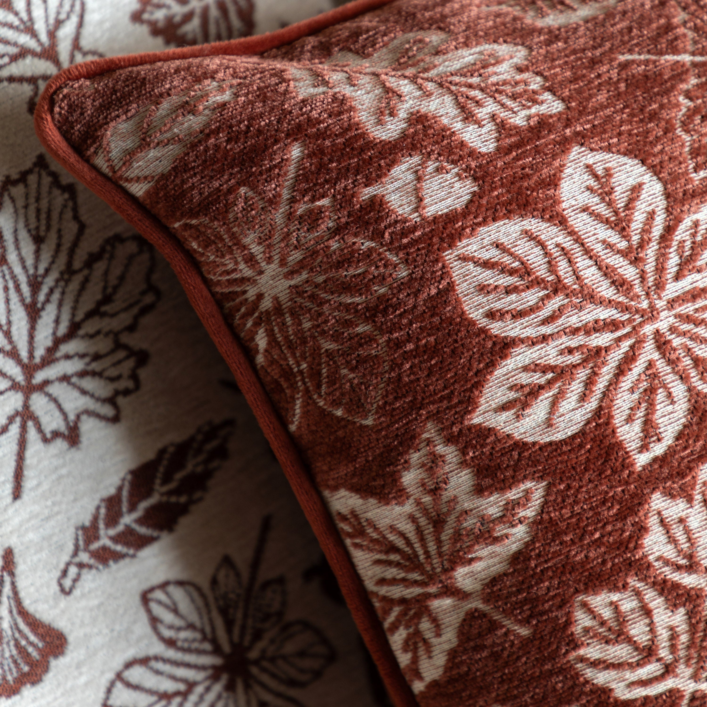 A close-up of the rust-colored cushion with white leaf patterns, showing the piping.