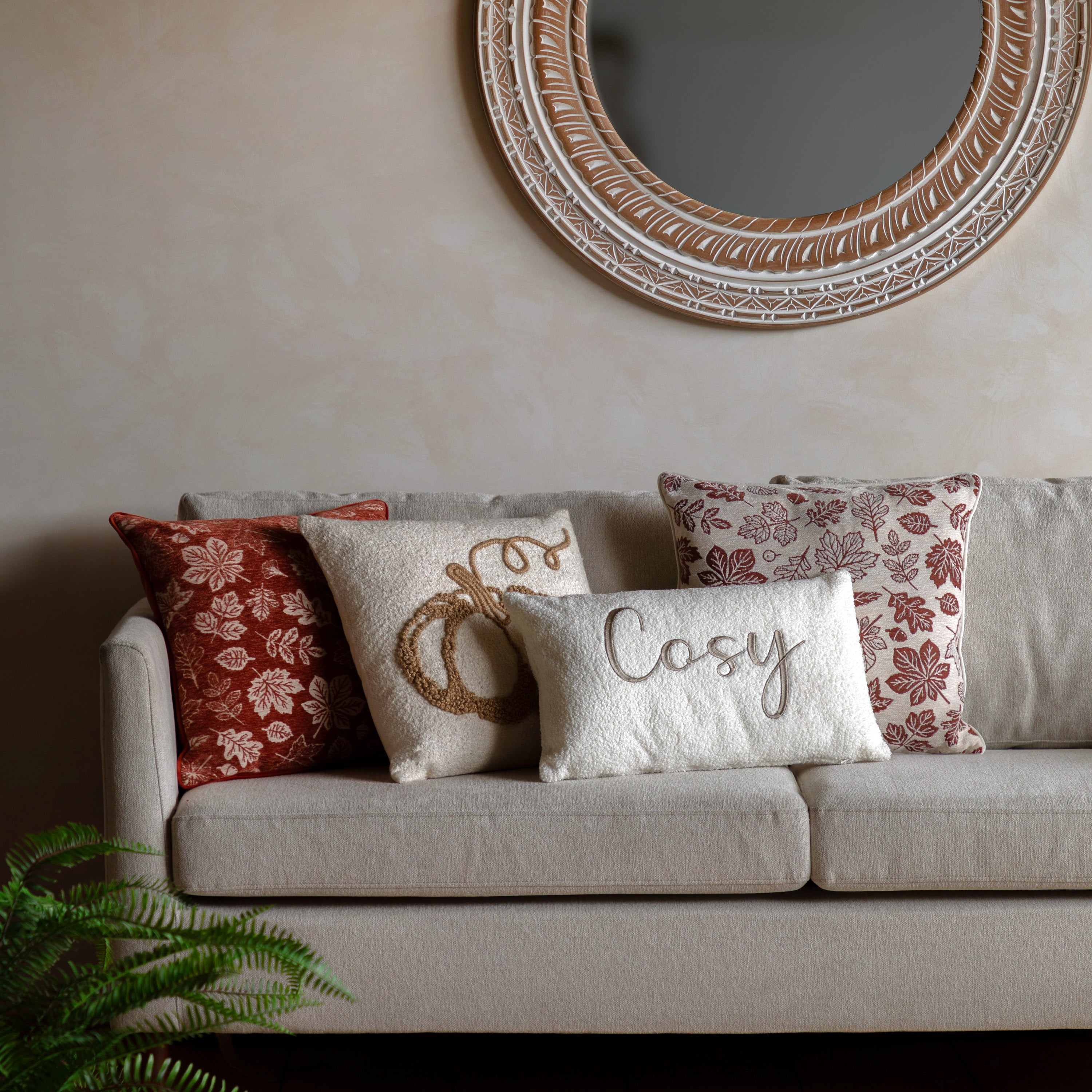A collection of autumn-themed cushions on a sofa with a round mirror above.