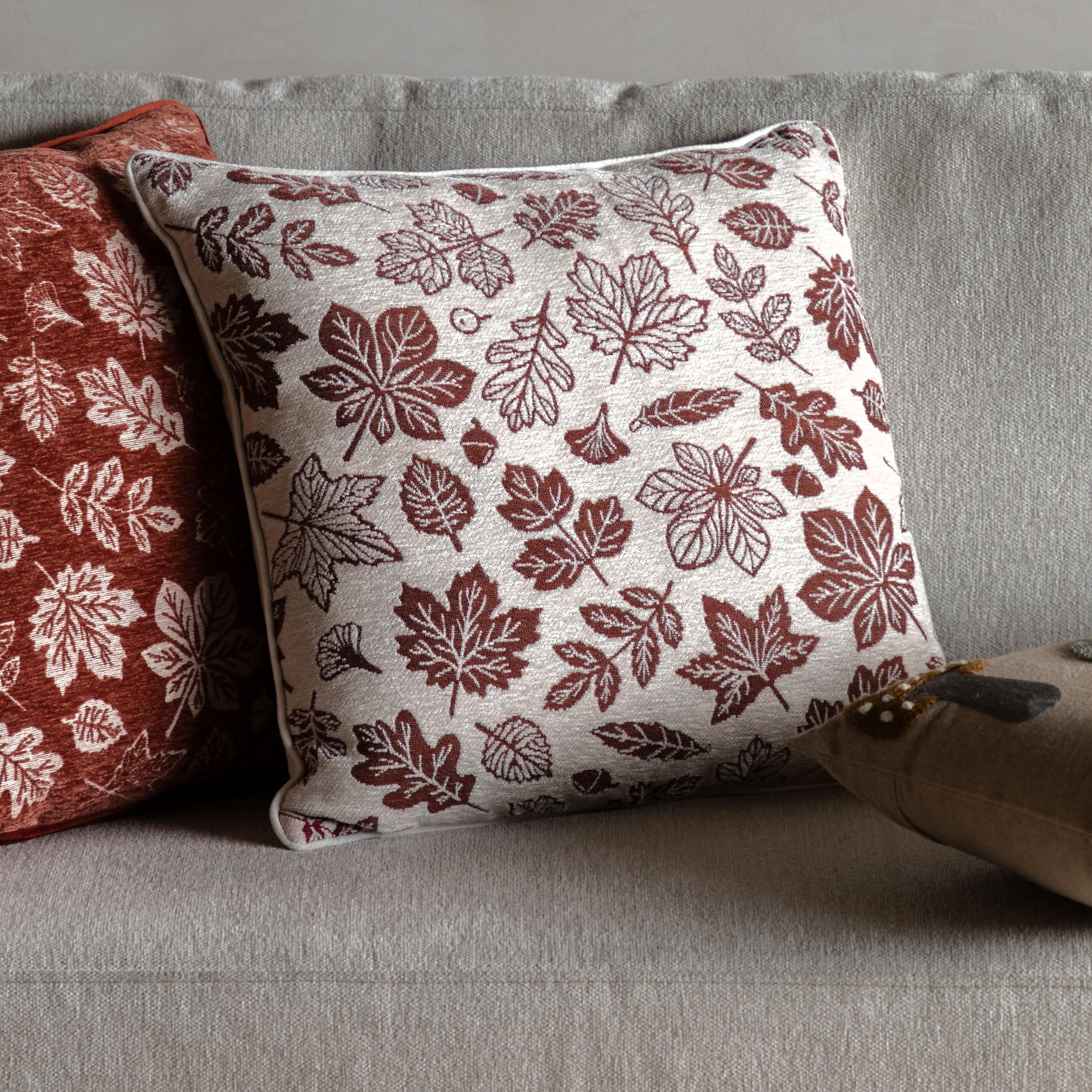 A close-up of a cushion with a cream background and red autumn leaf patterns.