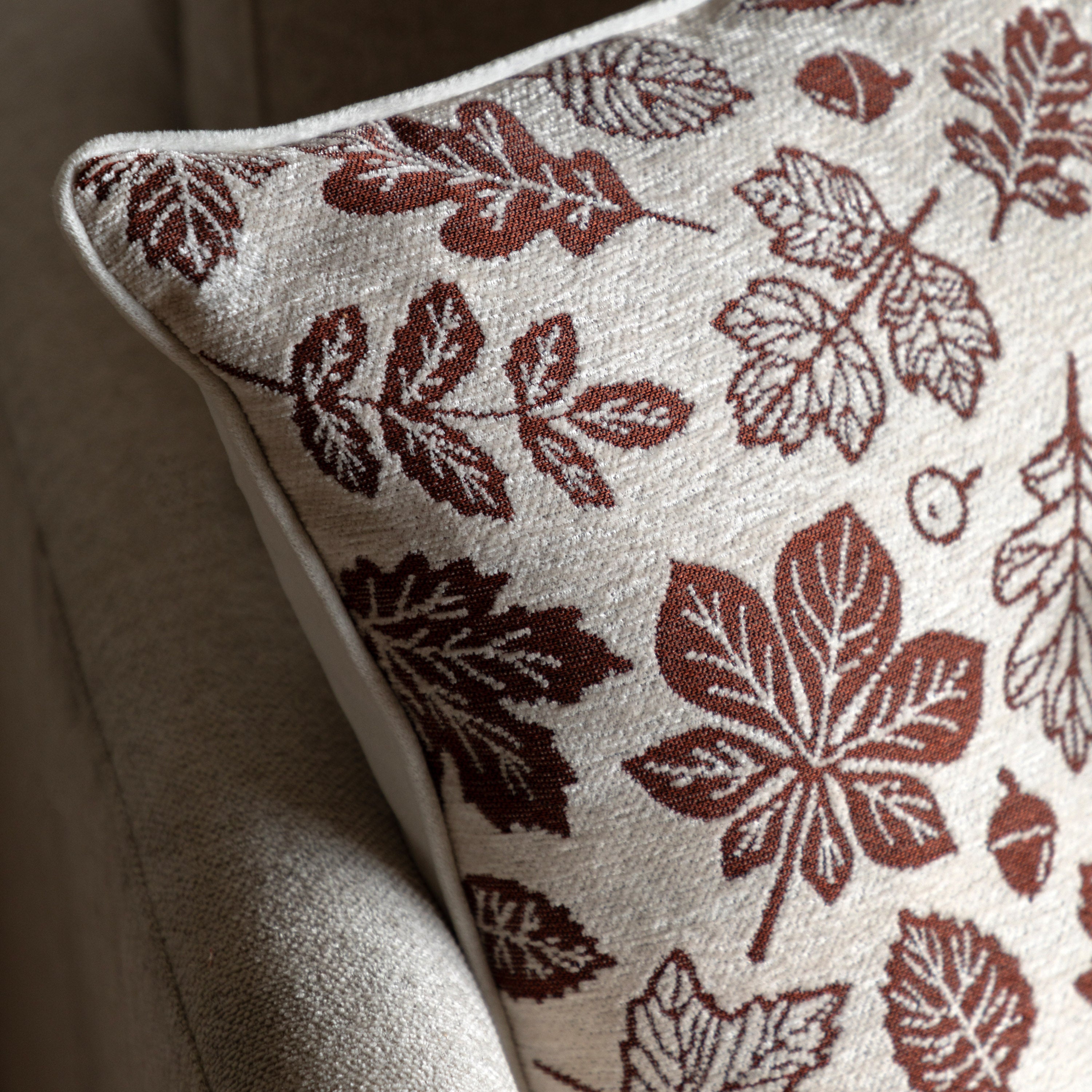 A close-up view of a cream cushion with a red autumn leaf pattern.