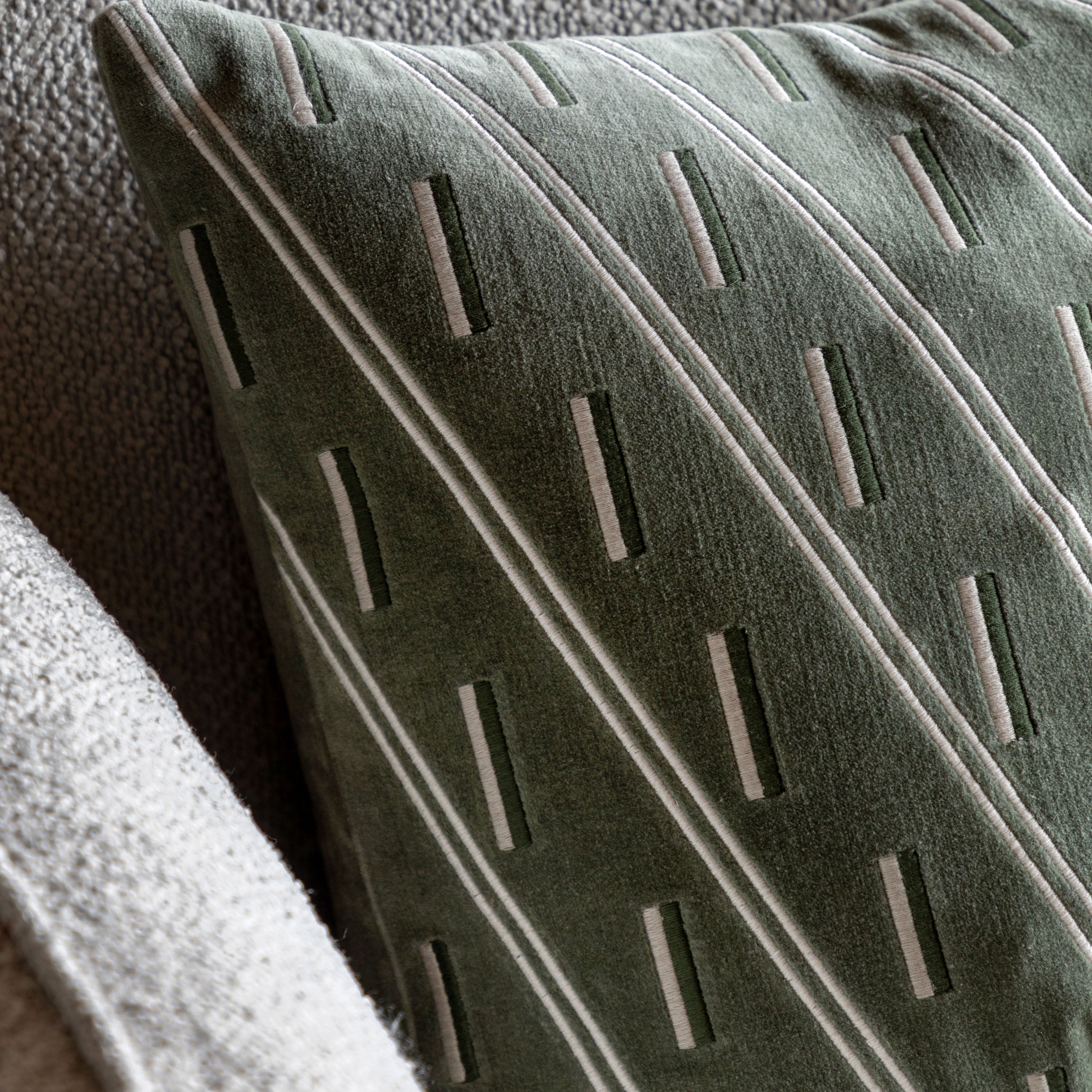 Close-up of olive green pillow with white stripes on a grey sofa.