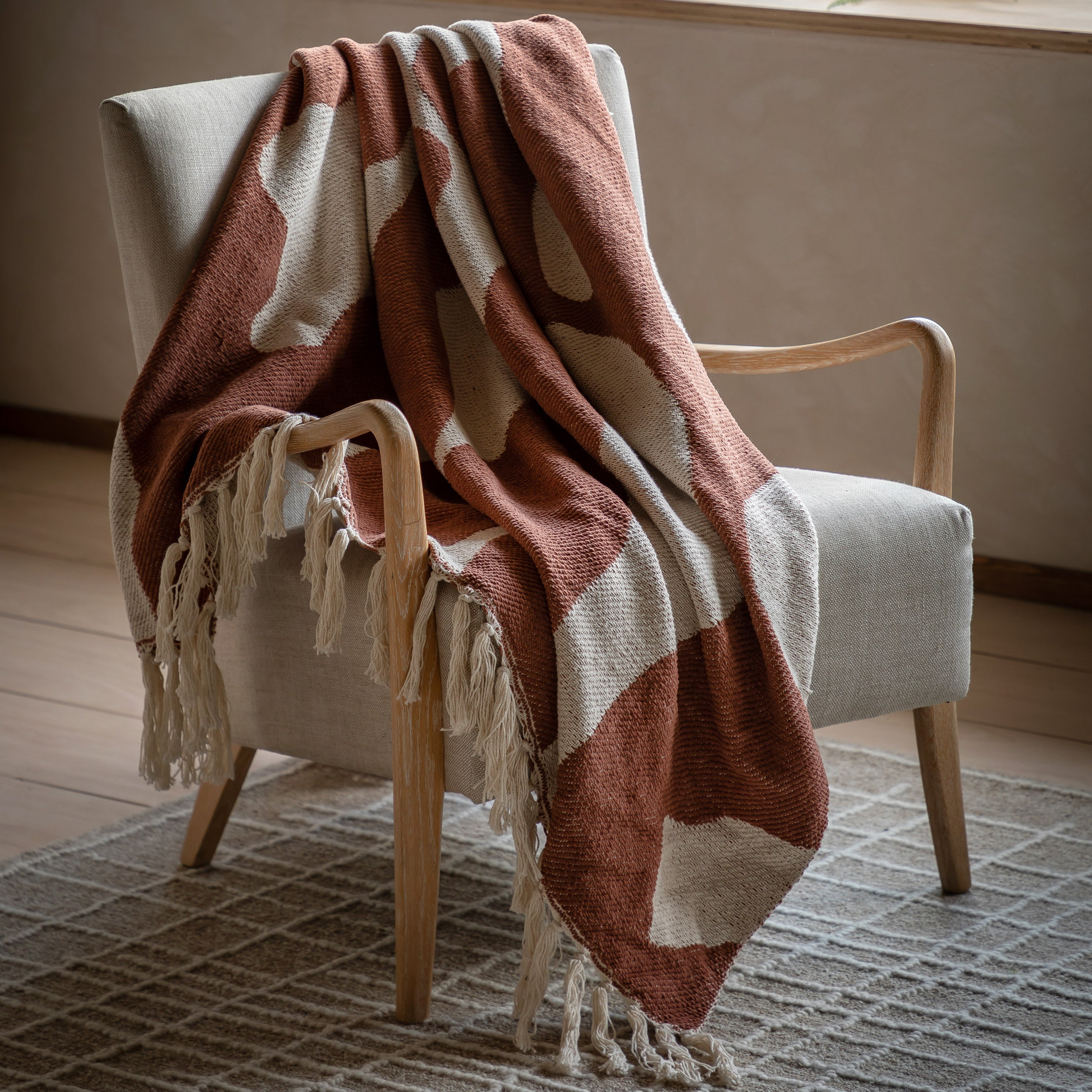 Boho throw blanket with burnt orange and off-white abstract pattern draped over a chair.