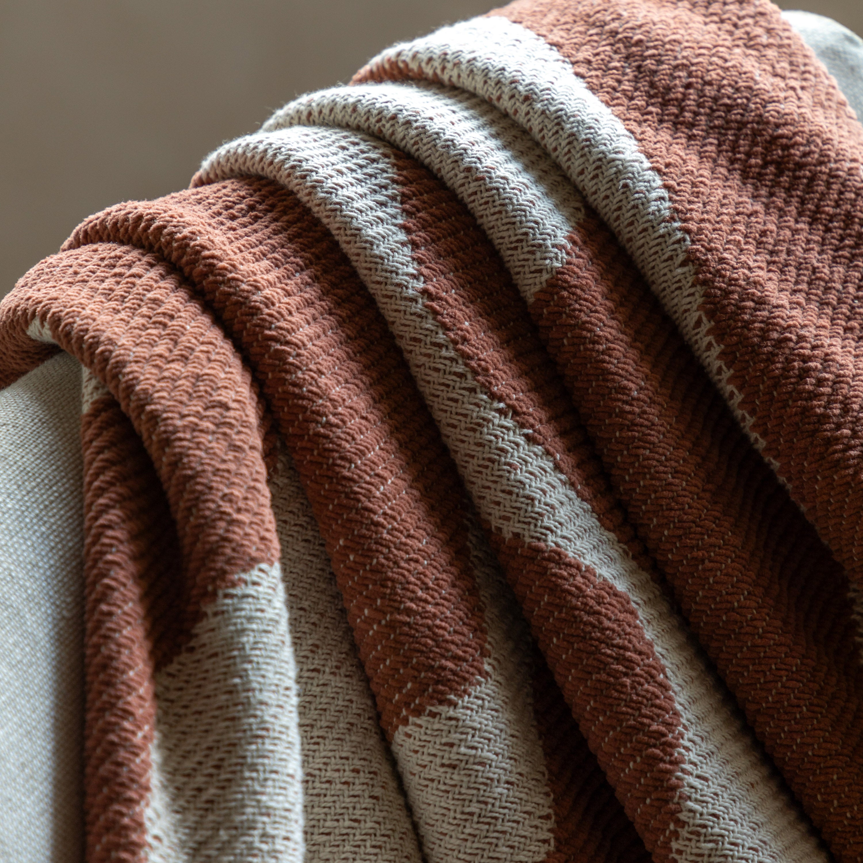 Close-up of a boho throw blanket with a burnt orange and off-white abstract pattern.