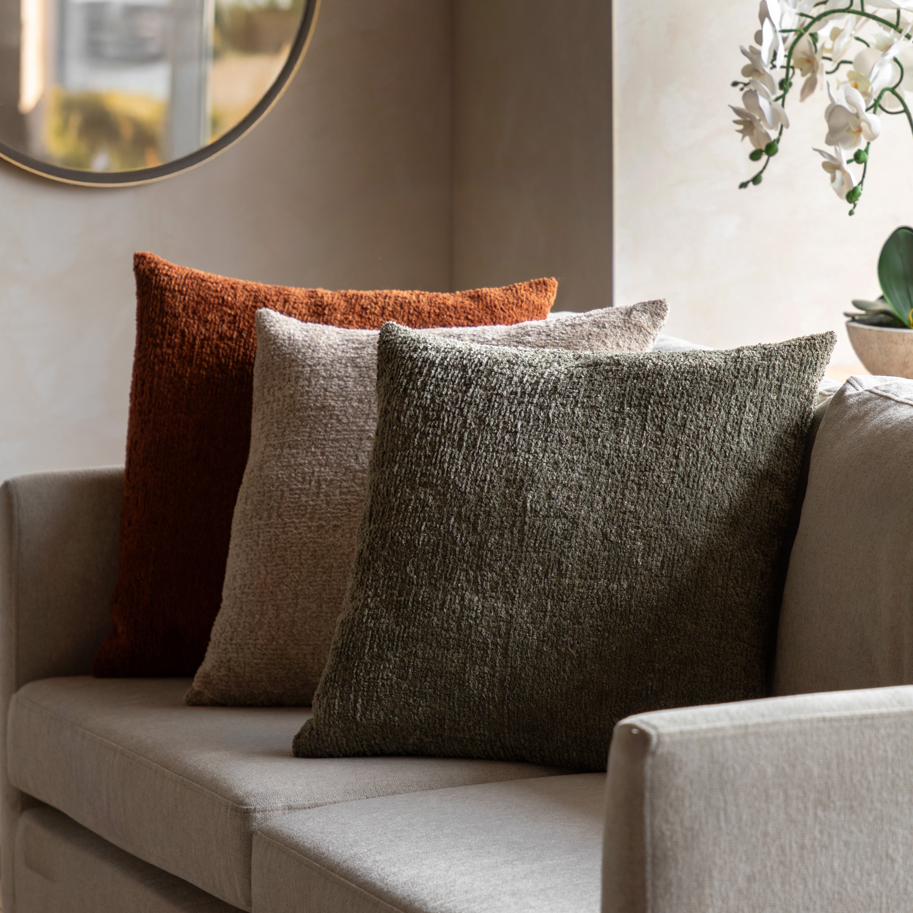 Three bouclé throw pillows in various colors on a modern sofa in a well-lit living room.