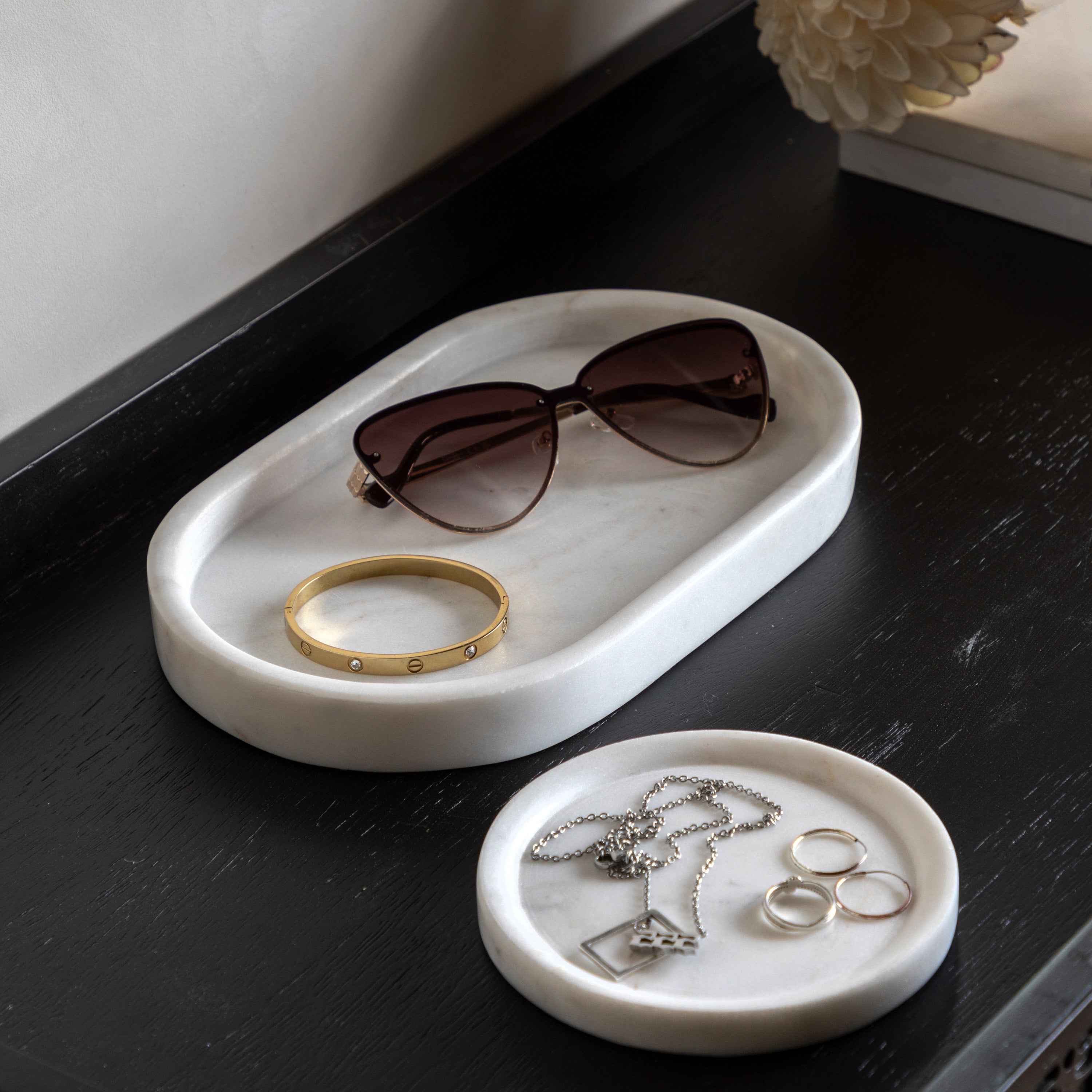 A large and a small marble tray hold sunglasses, a bracelet, rings, and a necklace.