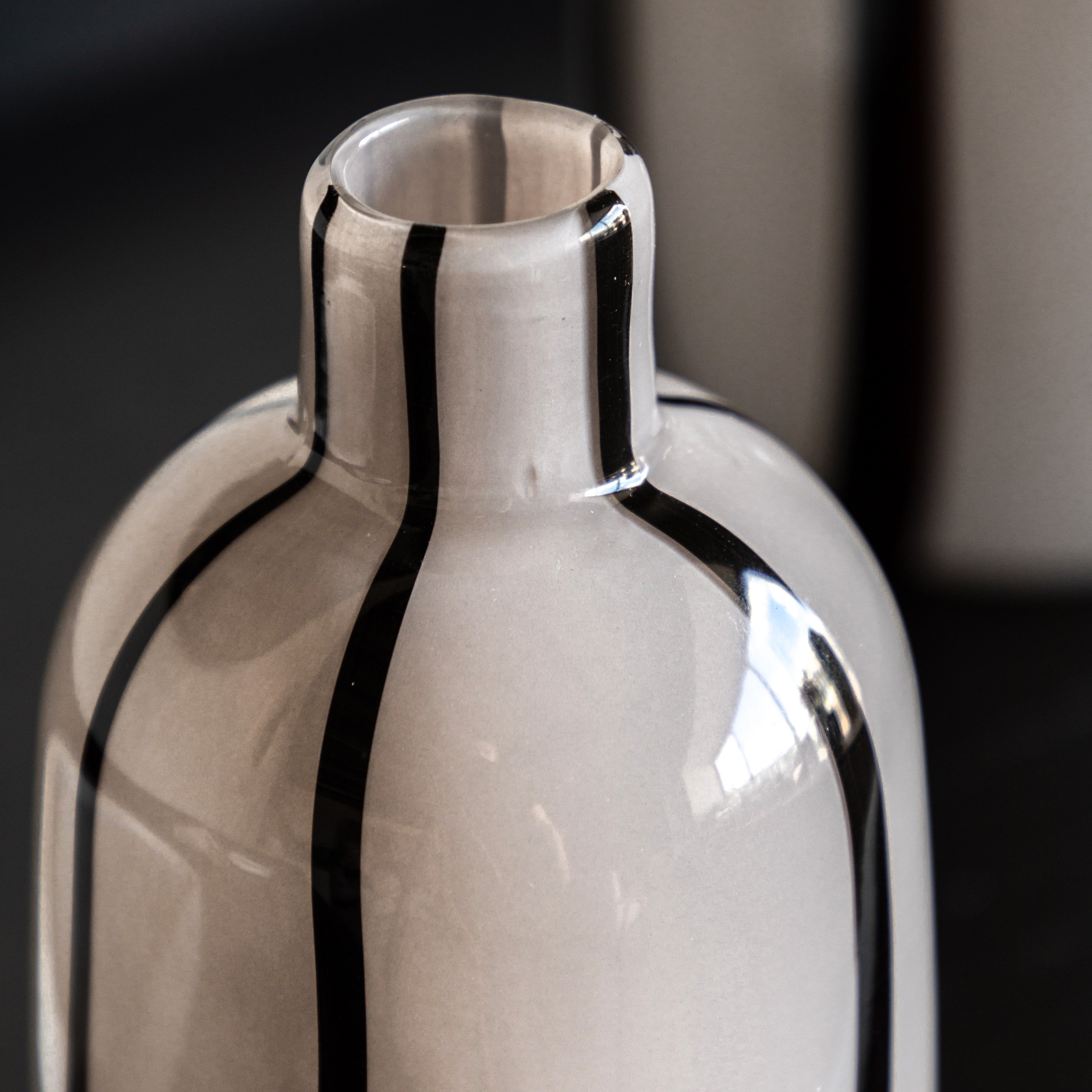 Close-up of the neck of an off-white vase with vertical black stripes.
