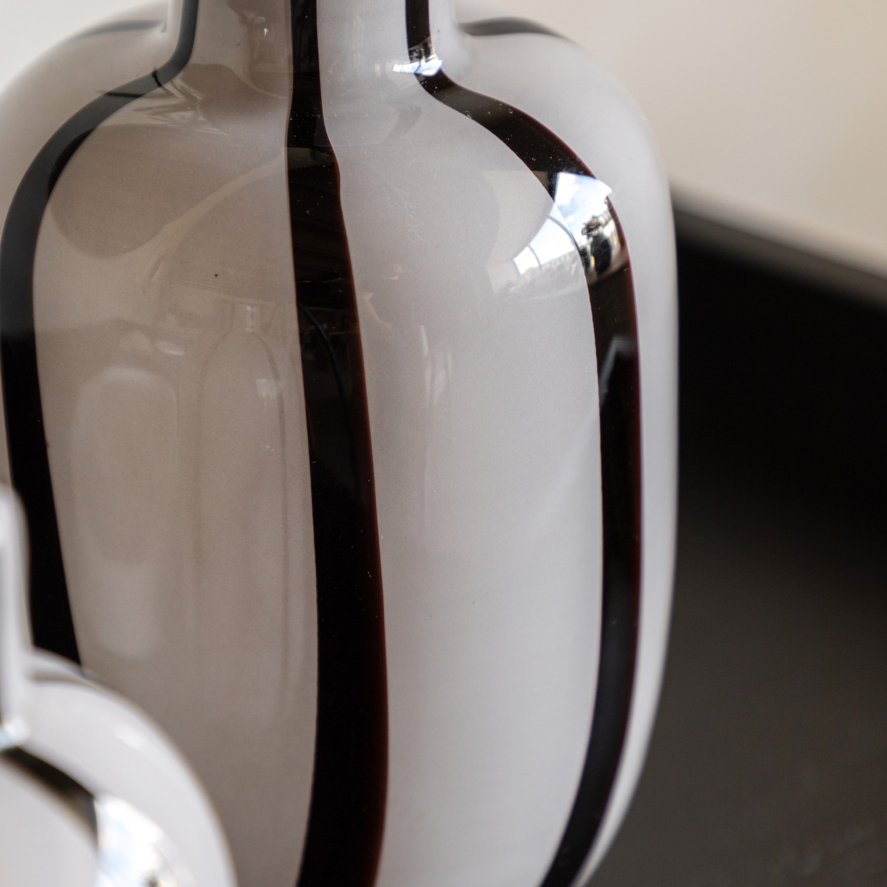 Close-up of the body of a striped off-white vase with black vertical lines.