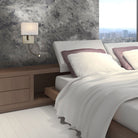 A modern brass wall light illuminates a stylish bedroom with a large bed and bedside table.