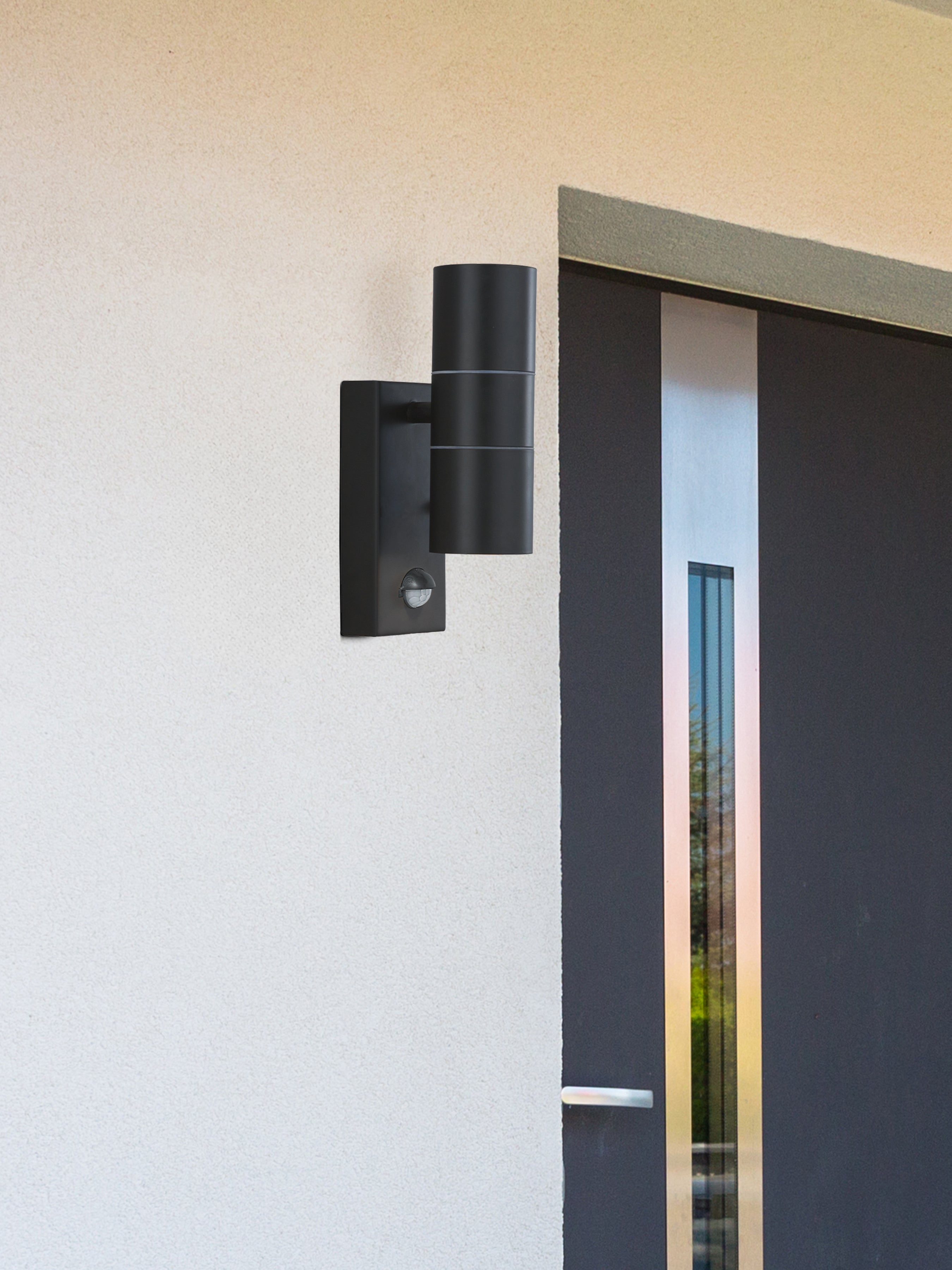 A black outdoor wall light mounted on a white wall next to a modern dark grey door.