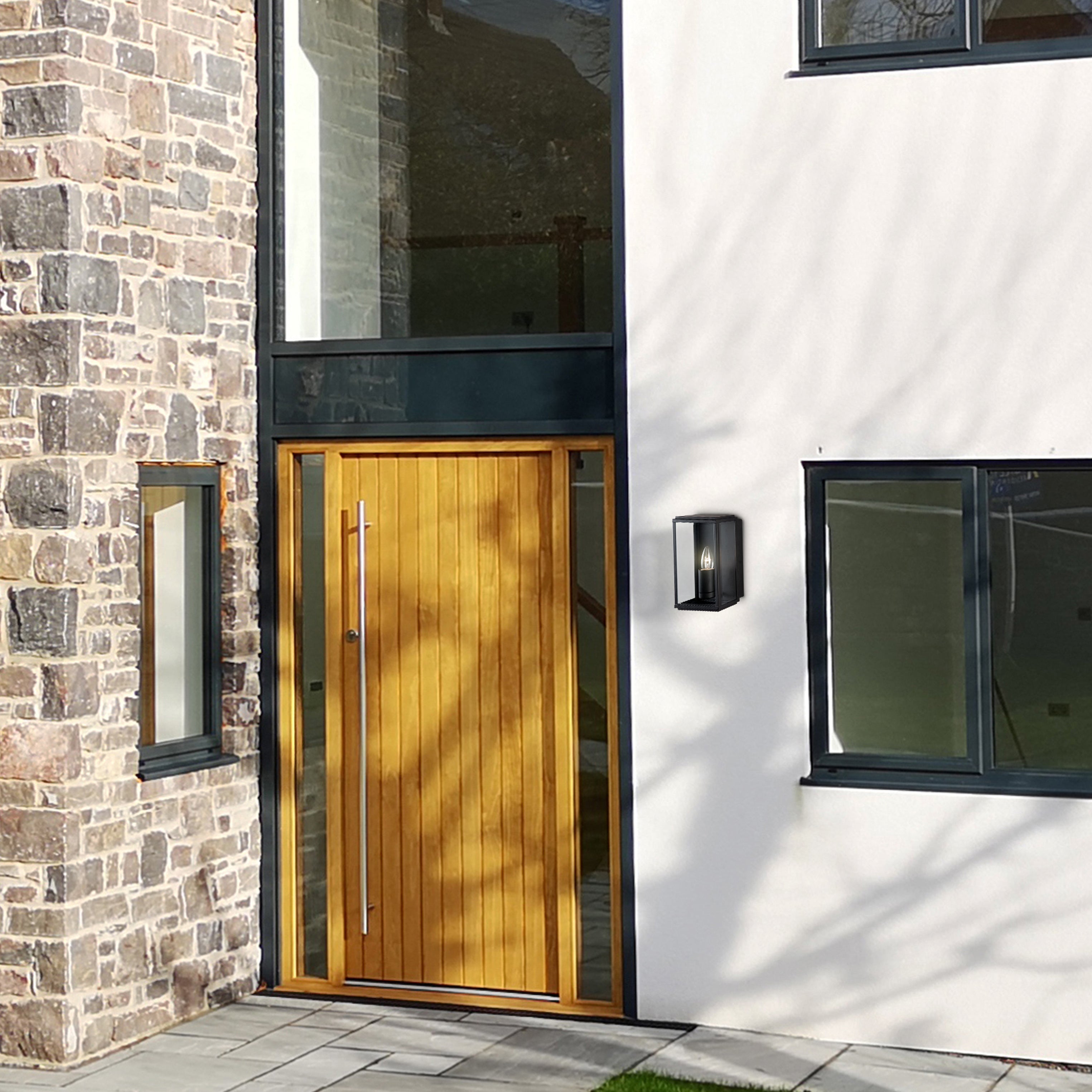 Black outdoor wall light installed on a modern white house exterior with a wooden door.