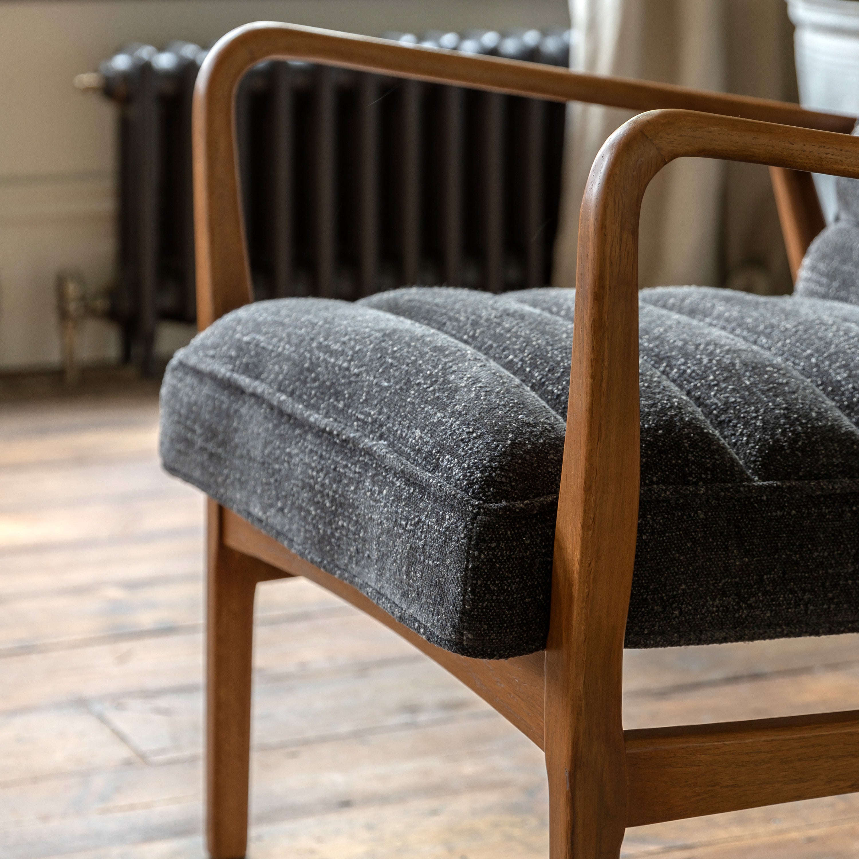 Close-up of the gray upholstered seat and wooden armrest of an armchair.