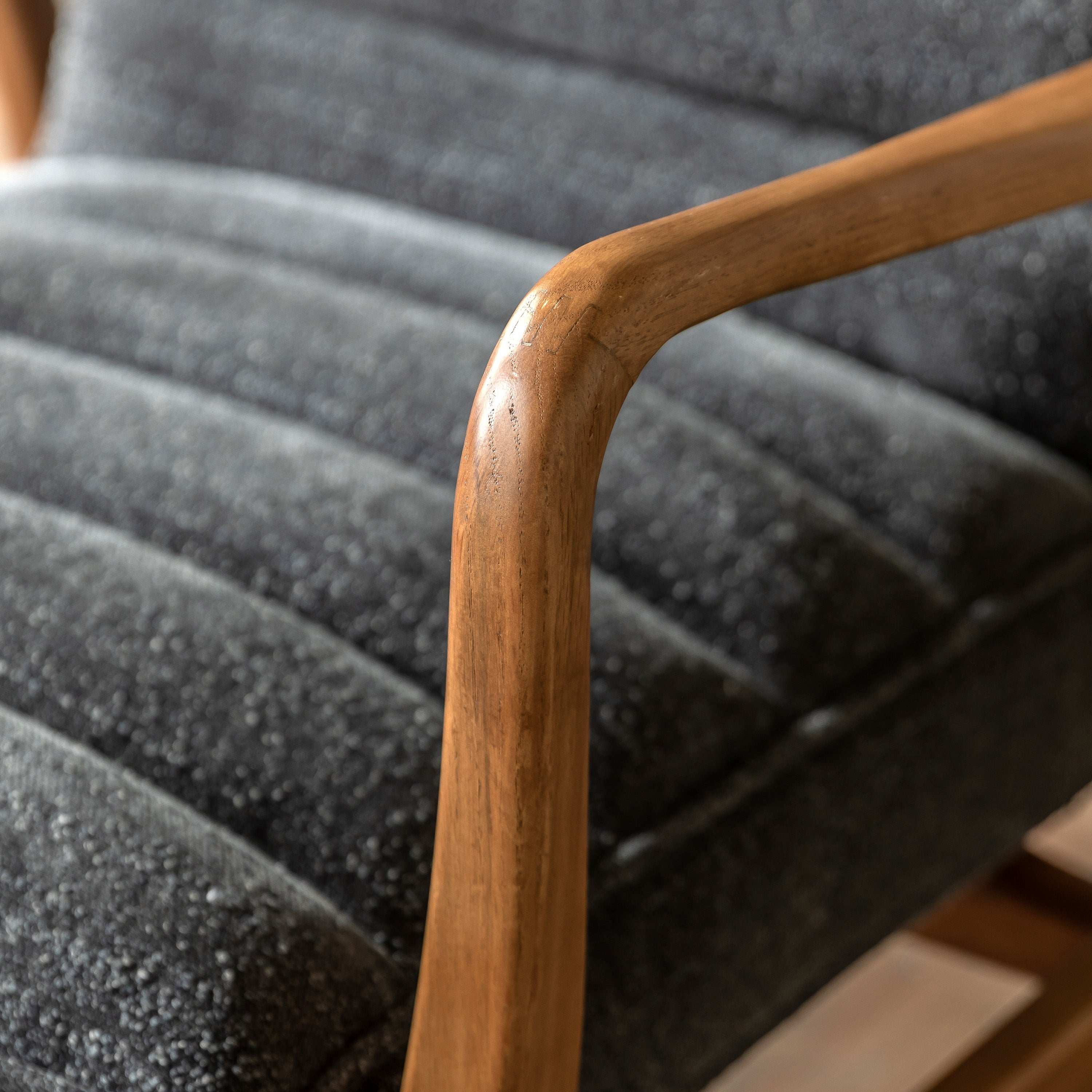 Detail of the wooden armrest and textured gray upholstery of an armchair.