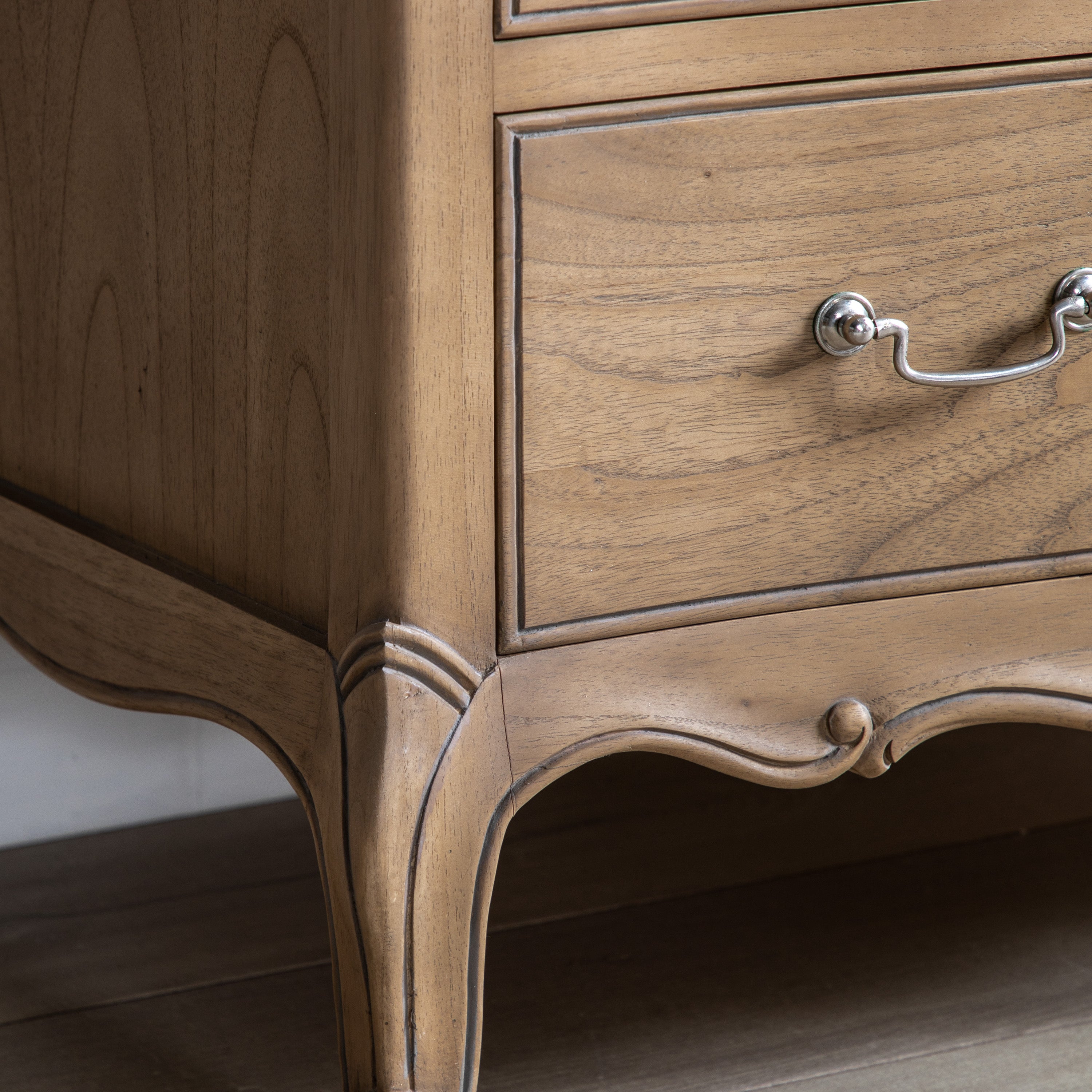 The bottom right corner of a wooden chest of drawers, showing an ornate leg and base.