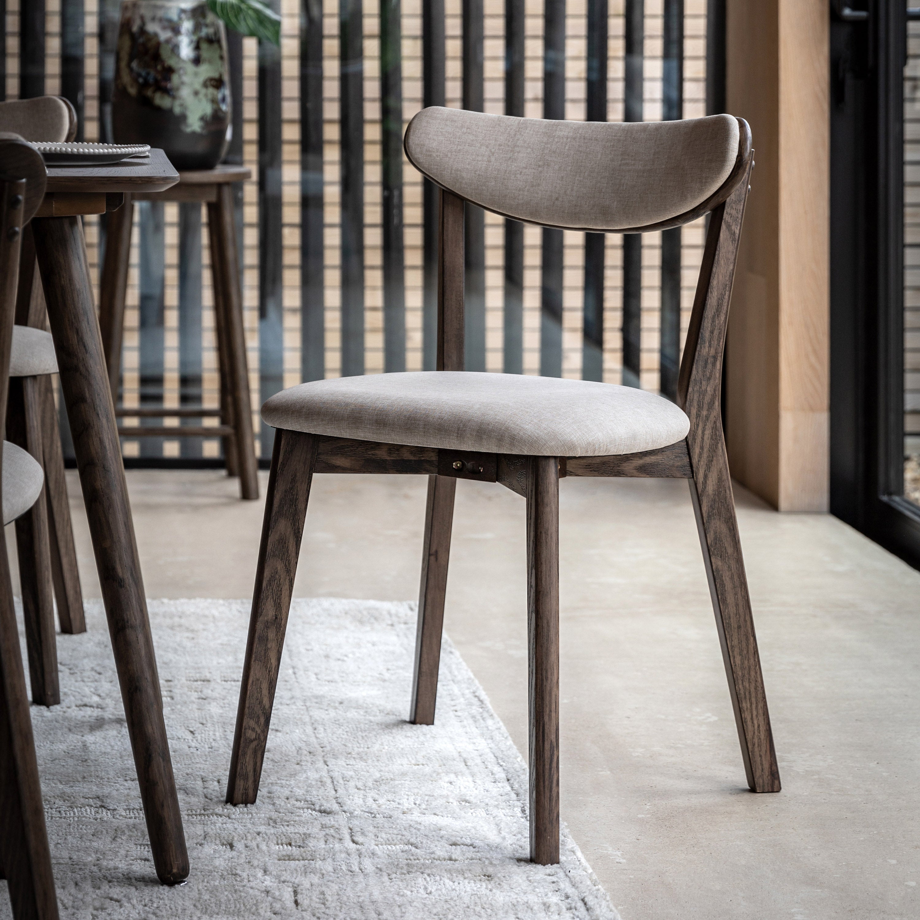 A close-up shot of a modern dining chair with a light upholstered seat and backrest.