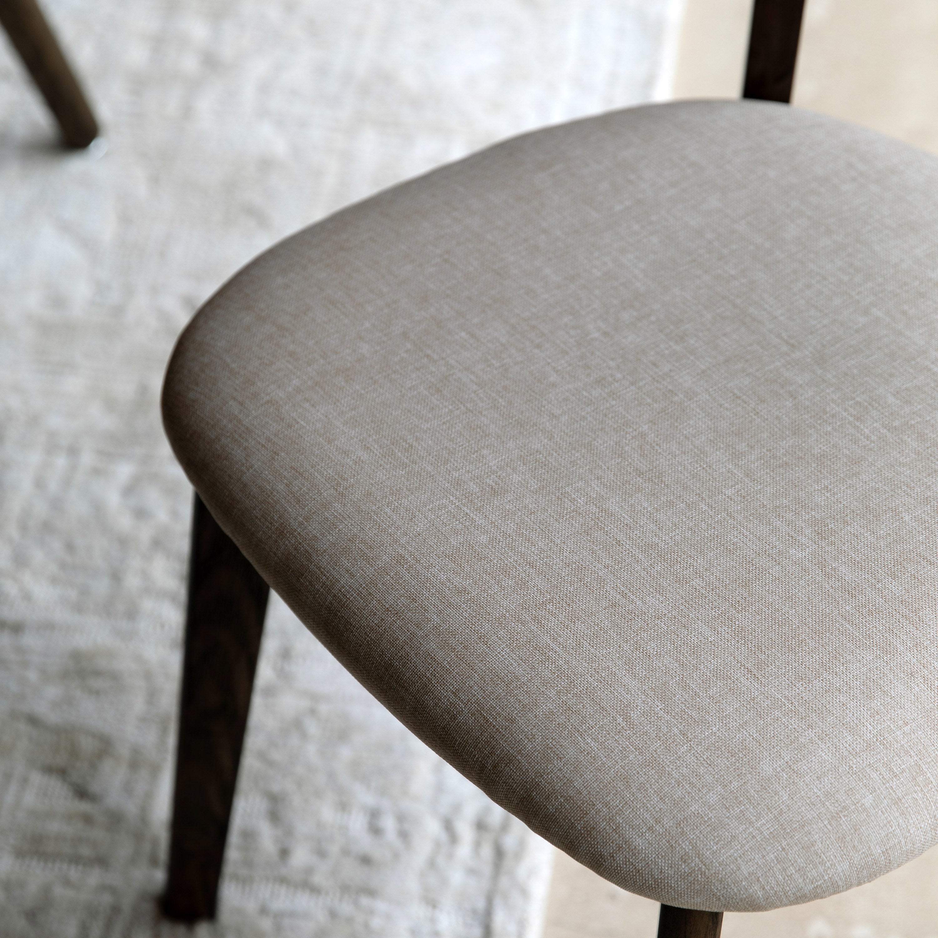 A close-up view of the light-colored, textured fabric upholstered seat of a dining chair.