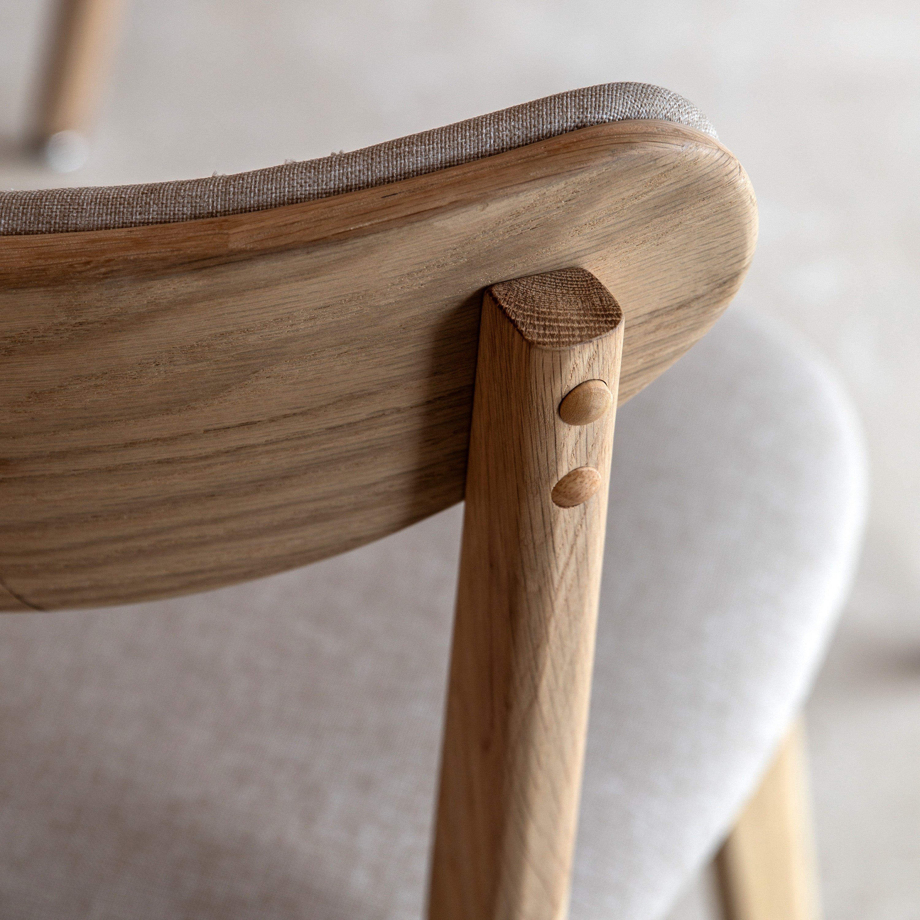 A close-up of the light wood and upholstered backrest of a dining chair.
