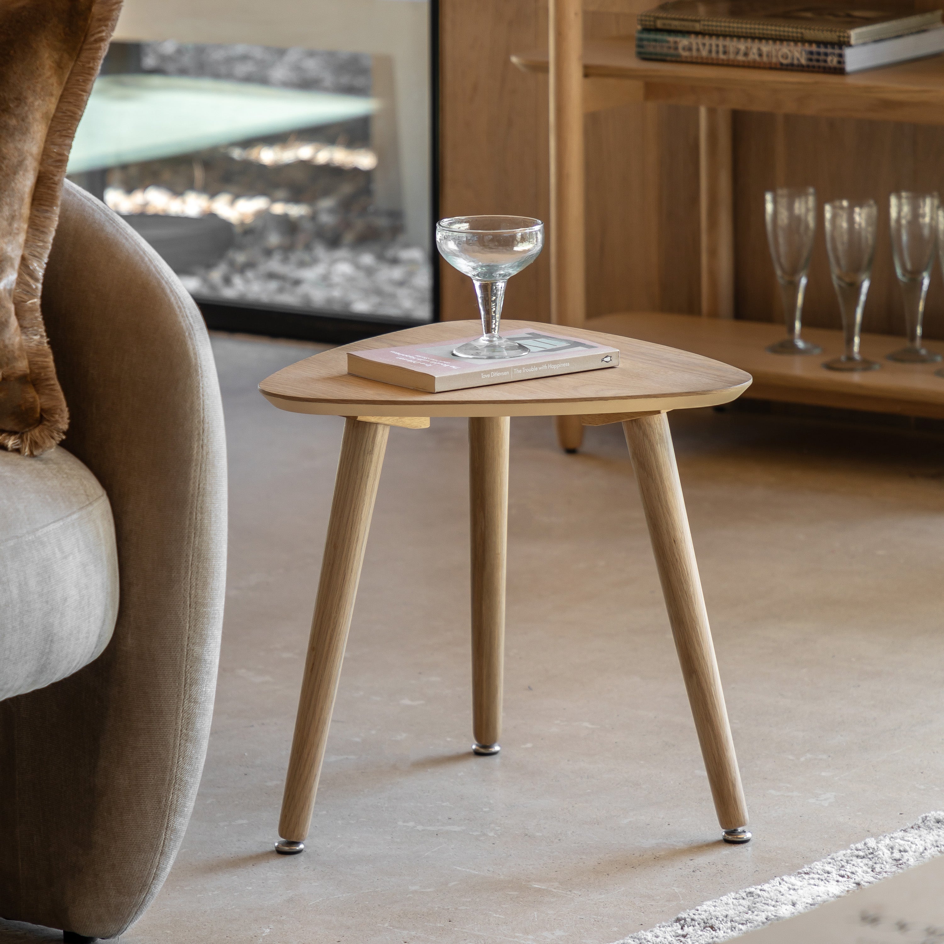 A triangular wooden side table with a glass of water and a book next to a sofa.