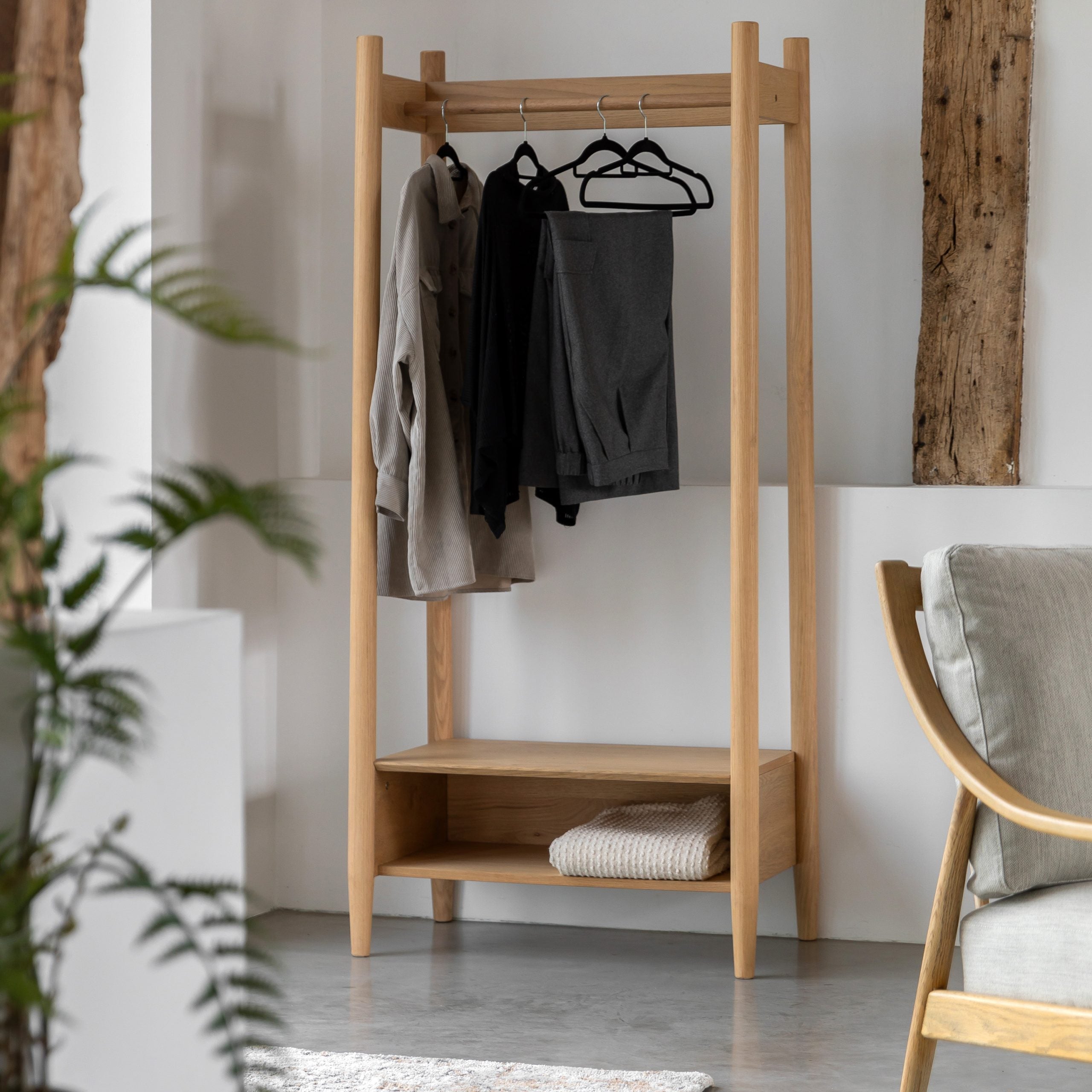A wooden clothing rack with clothes hanging on it, a blanket on the shelf, in a living room.