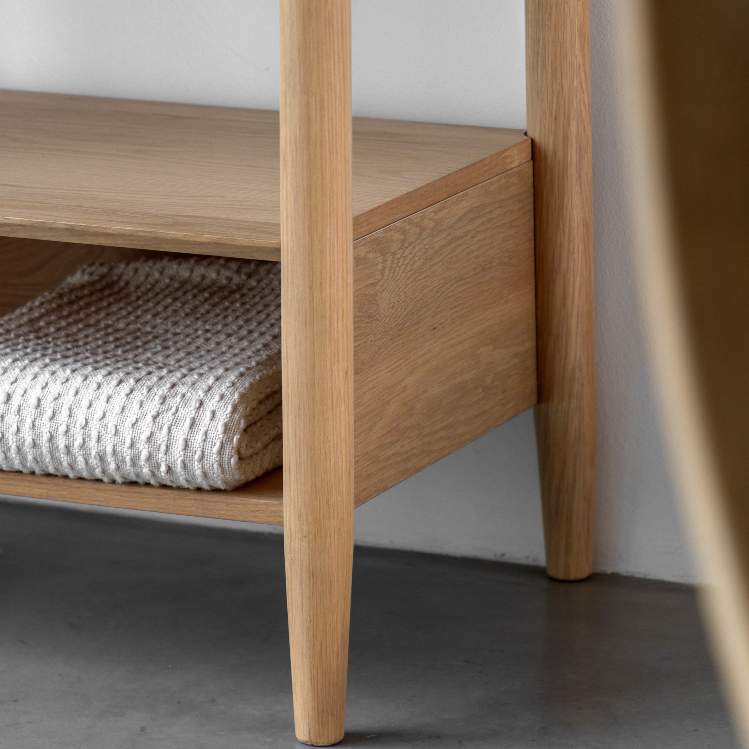 A close-up of the bottom shelf of a wooden clothing rack with a folded white blanket.