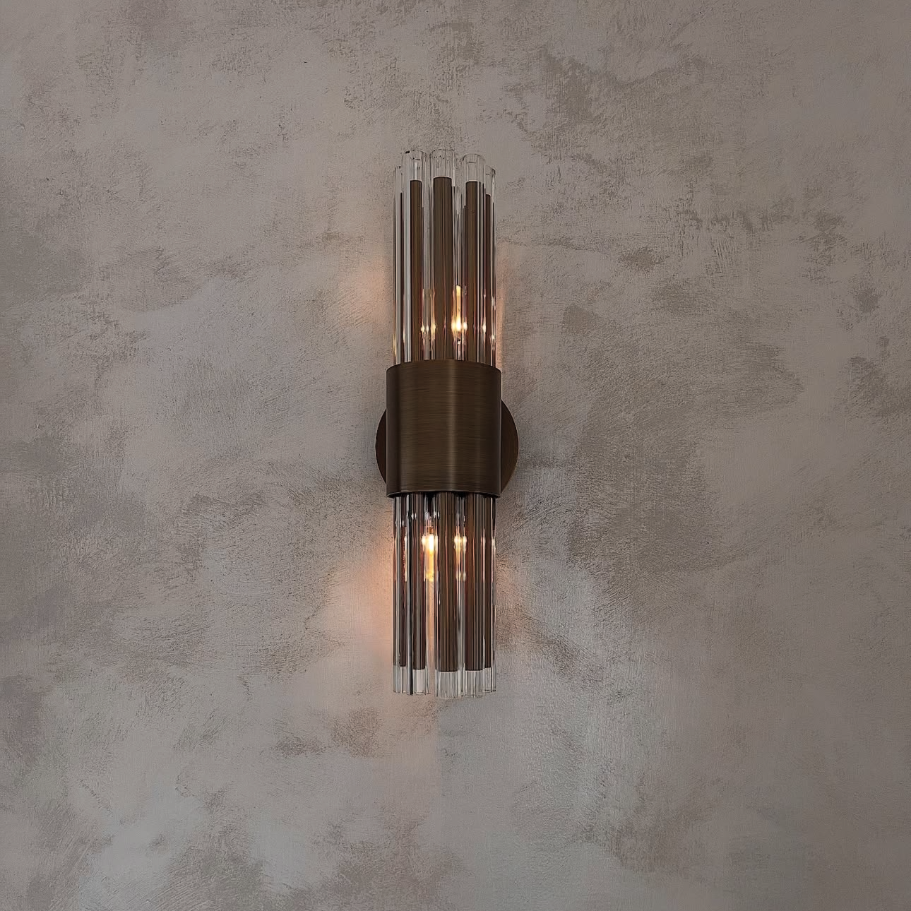 An illuminated brass and glass rod wall sconce casting warm light on a textured wall.