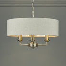 An elegant, cream fabric drum shade chandelier with three gold candle-style lights.