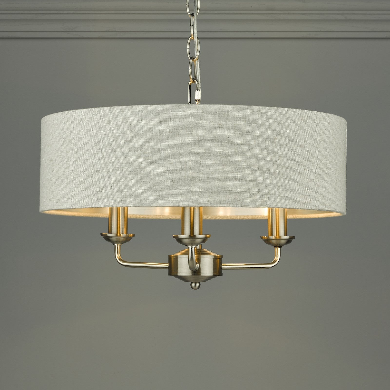 An elegant, cream fabric drum shade chandelier with three gold candle-style lights.